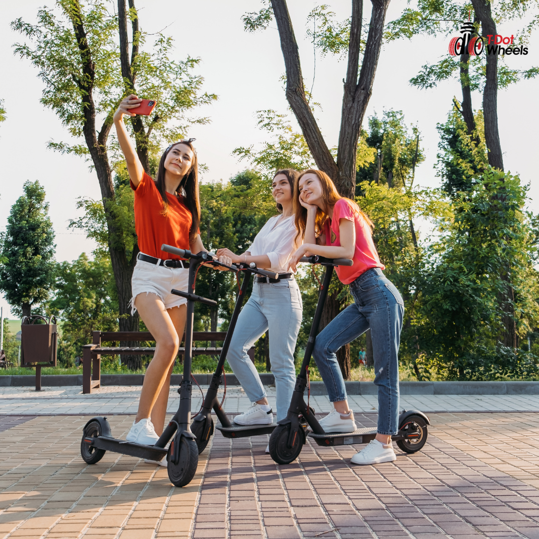 Three women taking a selfie while riding electric scooters in a park.