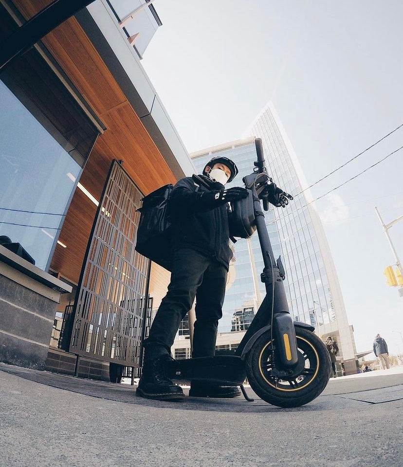 Delivery rider standing with an electric scooter outside a modern building