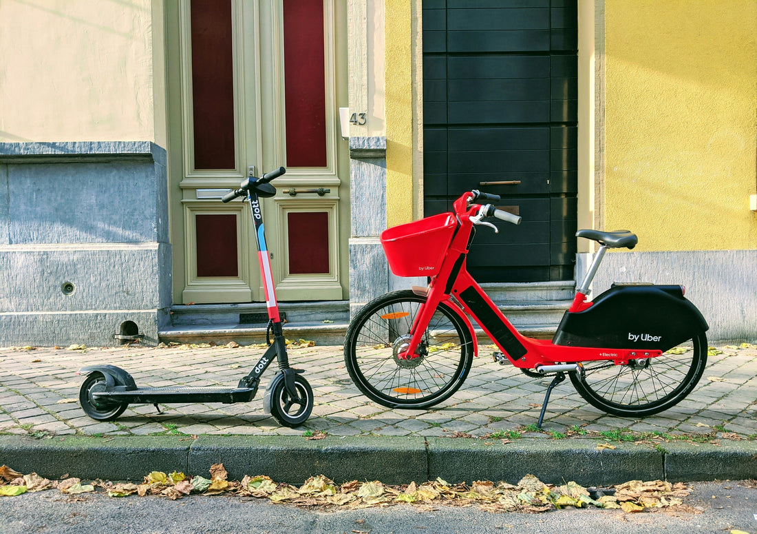 parked red electric bike and a black electric scooter side by side against an urban backdrop